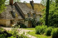 A charming English stone cottage with a moss-covered roof, climbing roses and a lush cottage garden