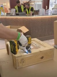 A technician opening a timber crate with a drill