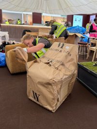 A Williams & Yates technician in gloves unwrapping a chair from its branded protective paper beside the olive tree